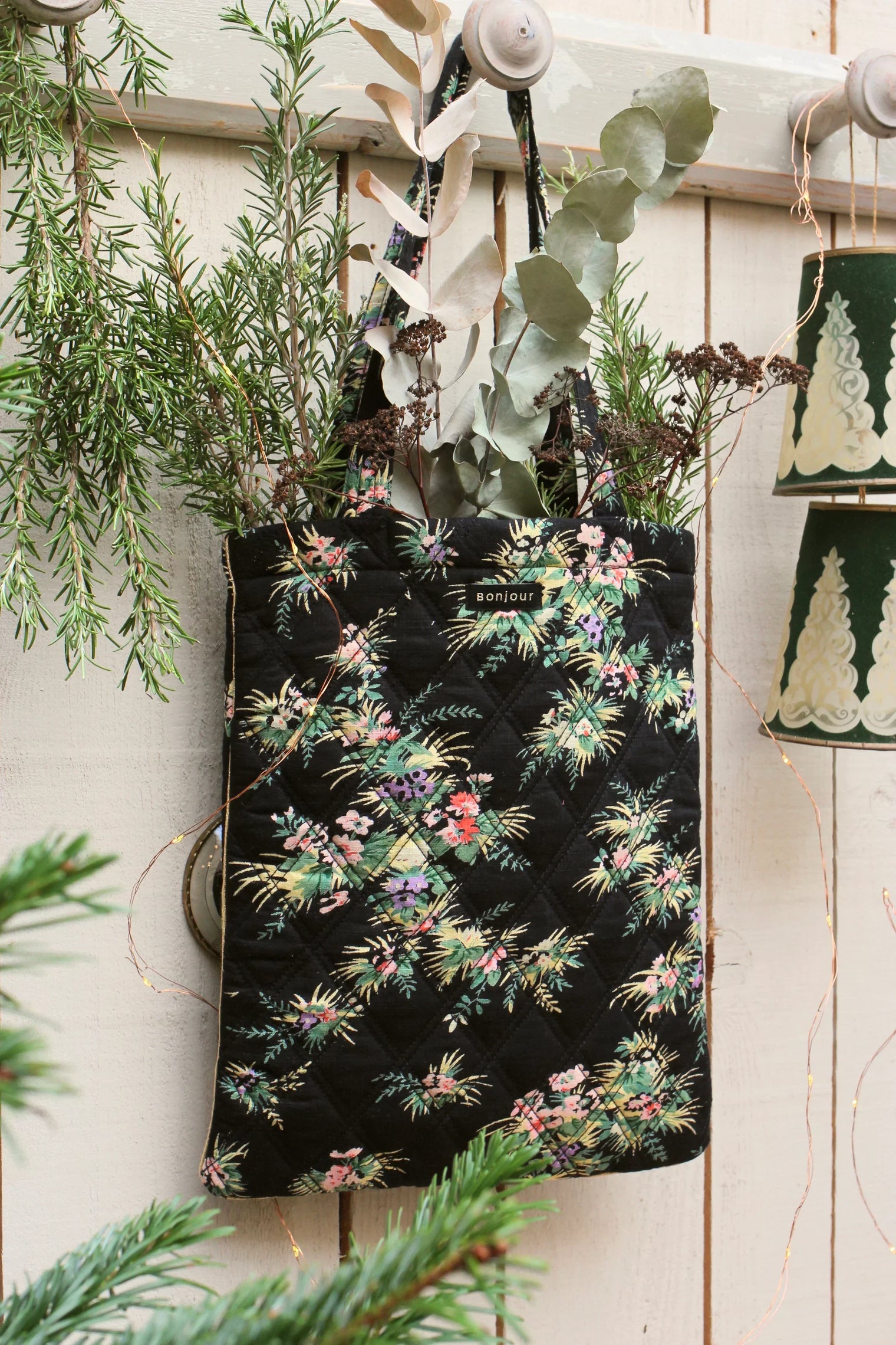 Quilted floral tote bag with botanical print, filled with greenery, hanging on wooden hook