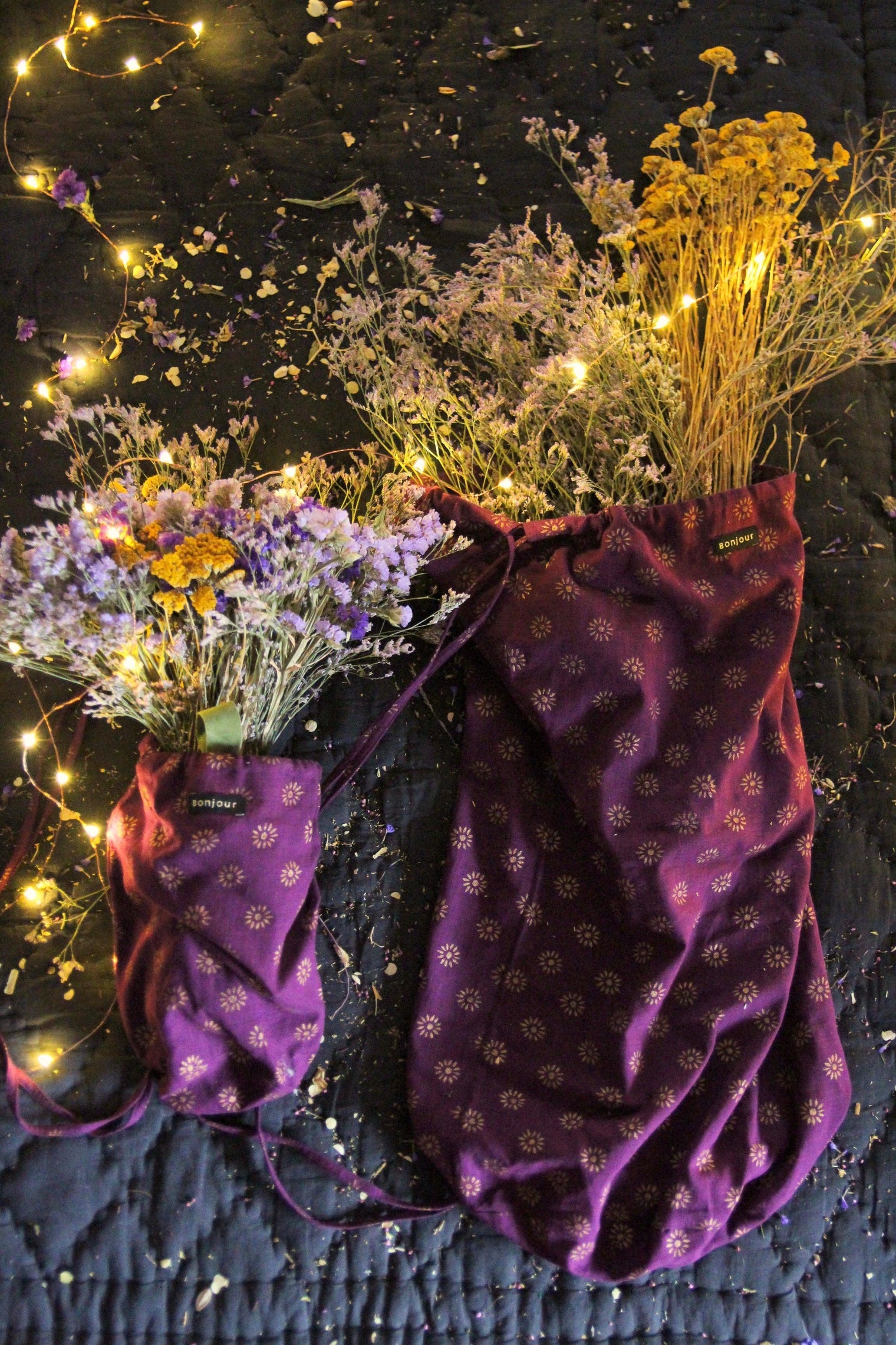 Purple floral print drawstring bags with dried flowers and fairy lights on dark quilted fabric