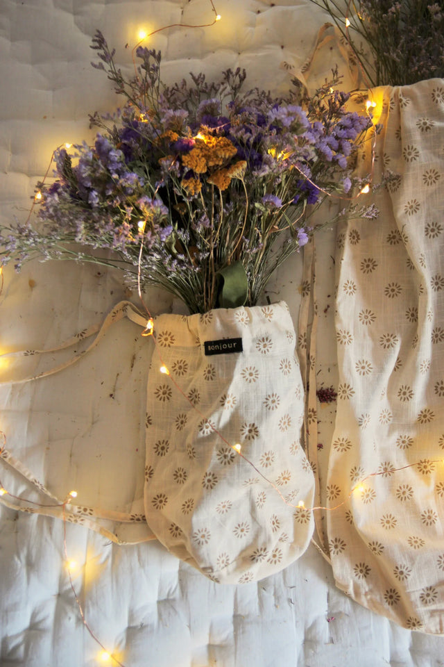 Floral print fabric pouch with dried purple and yellow flowers and warm string lights