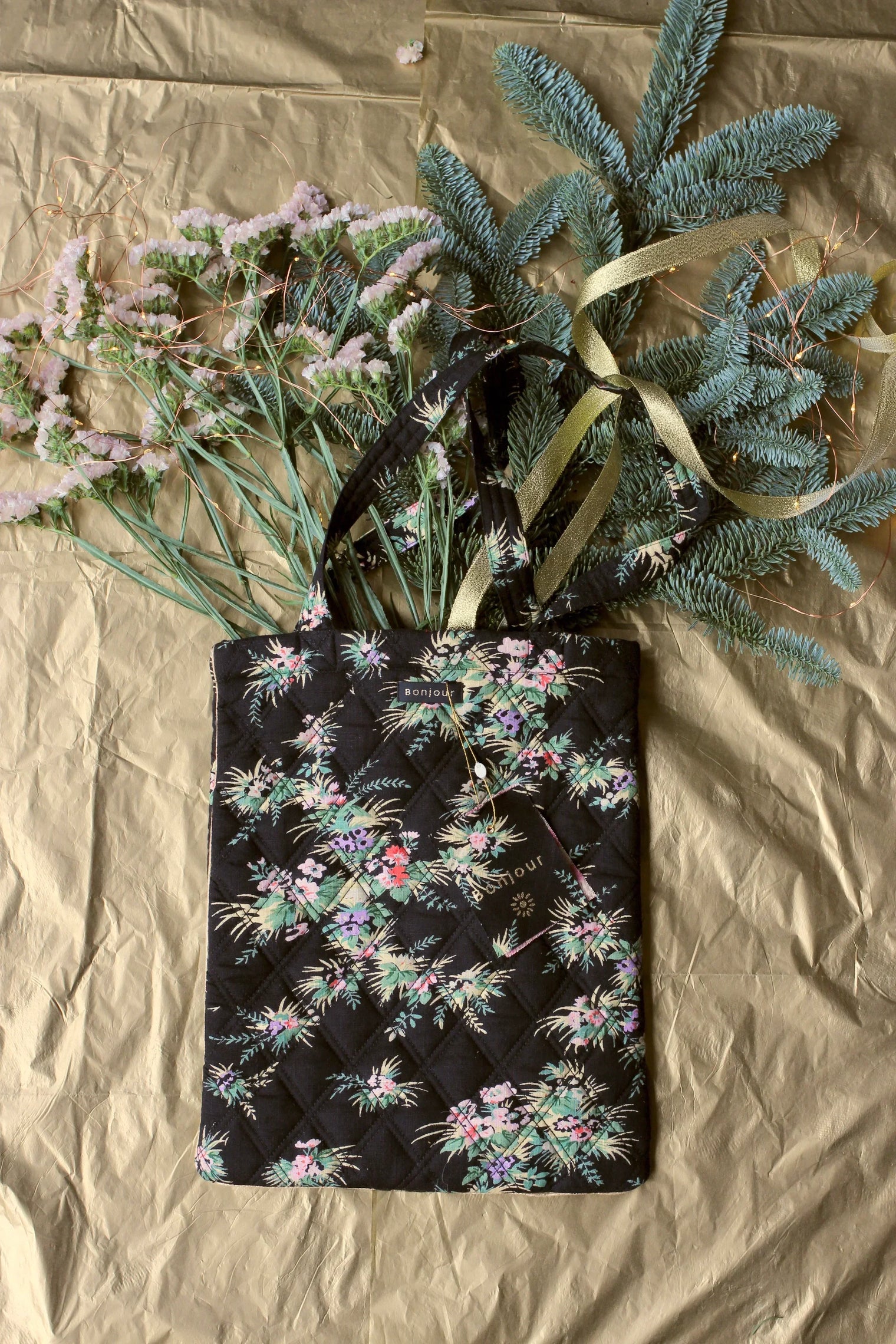 Quilted black floral tote bag with pastel flowers, styled with greenery on gold background.