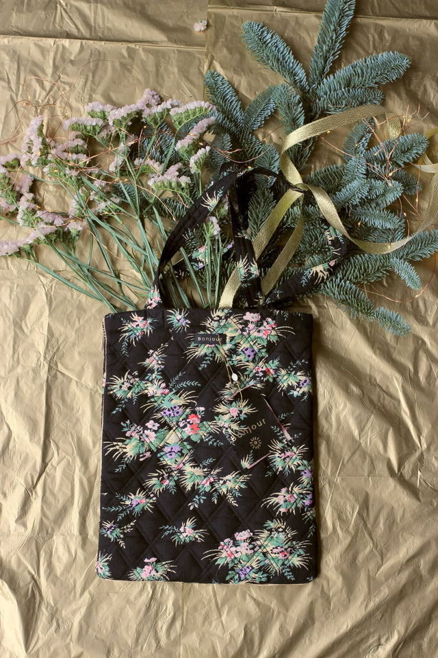 Quilted black floral tote bag with pastel flowers, styled with greenery on gold background.