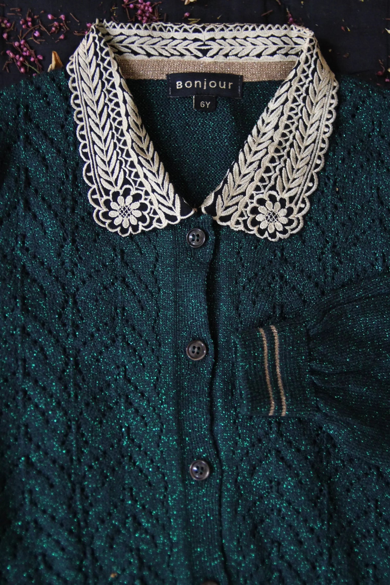Green knit children's cardigan with decorative cream embroidered collar and black buttons