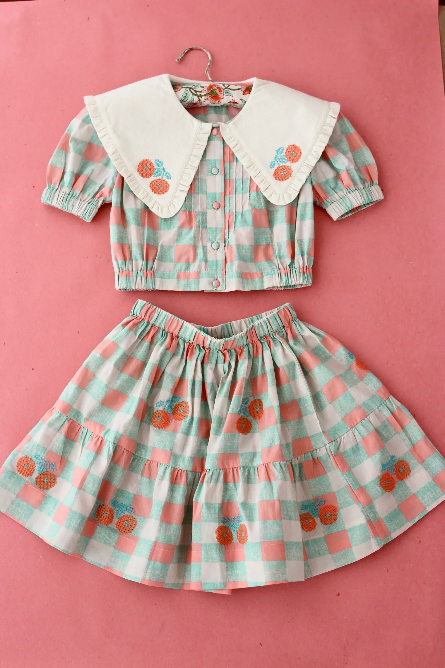Girls' checked skirt and blouse set with puff sleeves and embroidered flowers on pink backdrop