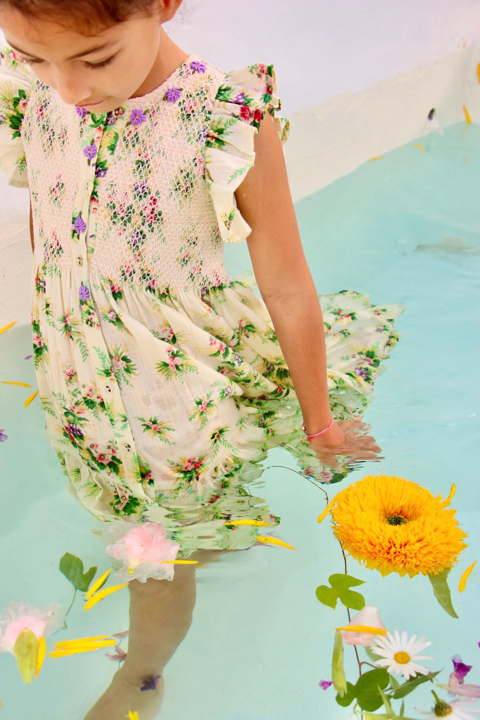 Girl wearing floral dress with ruffle sleeves standing in water with floating flowers