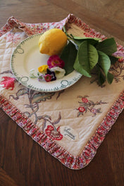 Suranné quilted placemat with floral print, a white plate, lemon, and fresh flower petals.