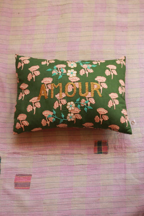 Green floral embroidered pillow with 'AMOUR' text on a pink patchwork quilt