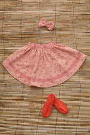 Pink floral girls skirt with matching bow hairclip and coral baby shoes on a bamboo mat
