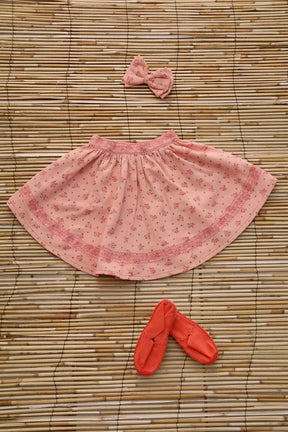 Pink floral girls skirt with matching bow hairclip and coral baby shoes on a bamboo mat