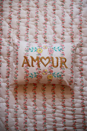 Floral embroidered pillow with 'AMOUR' text on matching floral quilted bedding