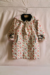 Floral print children's coat with black collar, front tie, contrast trim and pockets, hanging on a hanger.