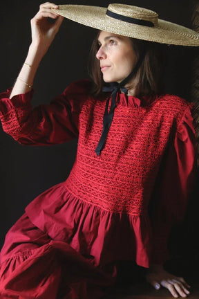 Woman in a red smocked dress with puff sleeves and straw hat with black ribbon