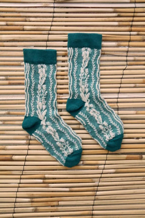 Green and cream floral knit children's socks on a bamboo mat background