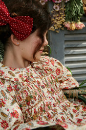 Girl in floral smocked dress with red polka dot hair bow, sitting beside dried flowers