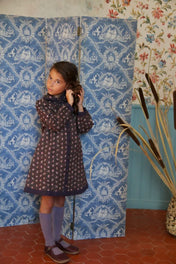 Young girl wearing a Bonjour quilted coat dress with floral print and purple tights.