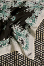 Floral print linen scarf with green and black details, laid on patterned fabric background