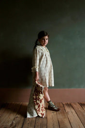 Girl in long-sleeved printed dress with lace collar holding patterned quilt on wooden floor
