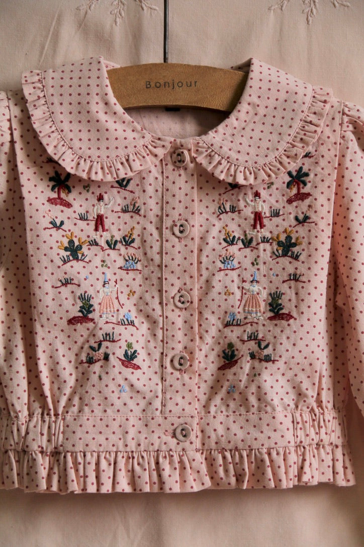 Embroidered blouse with small red polka dots on a pink background