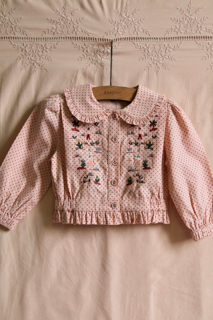 Embroidered blouse with small red polka dots on a pink background