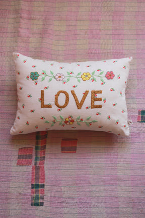 Embroidered decorative pillow with LOVE text and floral designs on pink patterned quilt