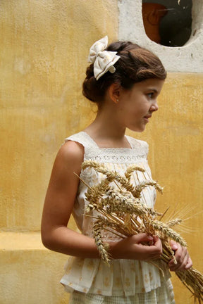 Girl in vintage-inspired sleeveless dress with bow hair accessory holding dried wheat stalks