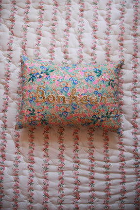 Floral embroidered pillow with "Happiness" text on patterned quilted bedding