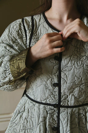 Woman buttoning striped quilted jacket with floral stitching and contrasting sleeve cuffs