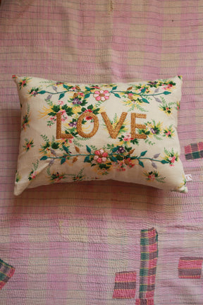 Embroidered decorative pillow with LOVE text and floral design on pink quilted bedding