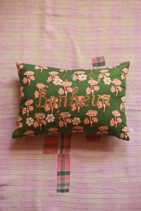 Green floral embroidered cushion with "happiness" on a pink quilted bedspread