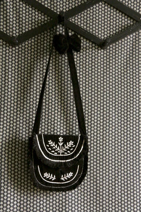 Black velvet embroidered shoulder bag with floral pattern hanging on patterned wall hook