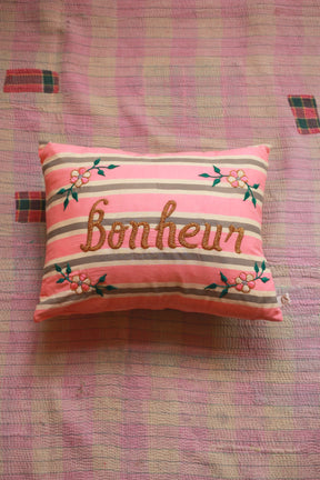 Pink striped cushion with embroidered Bonheur text and floral accents on quilted blanket