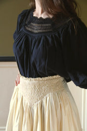 Woman wearing a black lace blouse with a high-waisted smocked cream skirt