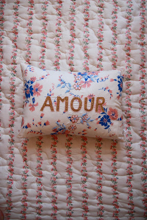 Floral embroidered pillow with 'AMOUR' text on a quilted floral bedspread