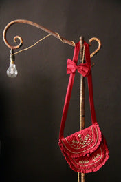 Red embroidered children’s bag with ruffles and bow hanging on rustic hook