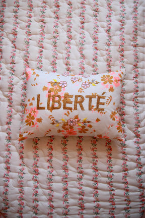 Floral embroidered pillow with 'LIBERTÉ' text on quilted, floral-print bedding