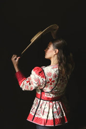 Woman in floral quilted jacket with red accents holding straw hat against dark background