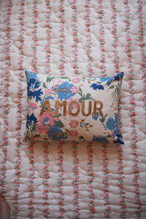 Floral embroidered cushion with "AMOUR" text on a pink floral quilt, decorative home linen