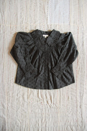 Black long sleeve children's blouse with lace collar and cuffs on a quilted background