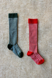 Two pairs of striped knee-high kids' socks, one green and one red, on textured fabric
