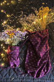Purple floral print drawstring bags with dried flowers and fairy lights on dark quilted fabric