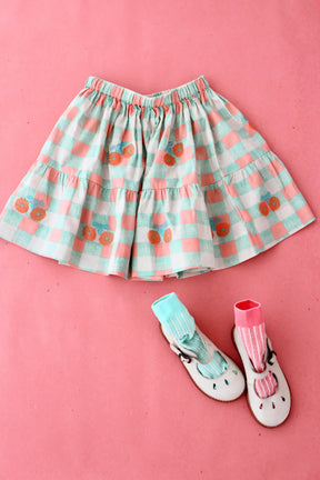 Girls’ pastel gingham skirt with floral embroidery, kids’ shoes and socks on pink background